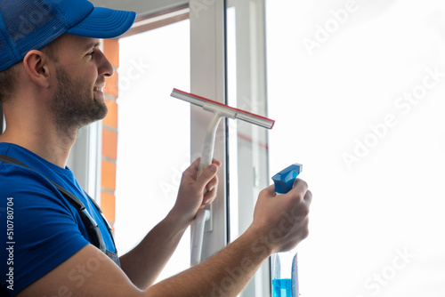 Canvas Print Worker in blue uniform cleans plastic window with detergent and squeegee
