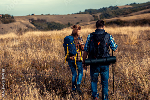 Couple with backpacks hiking together in nature on autumn day.