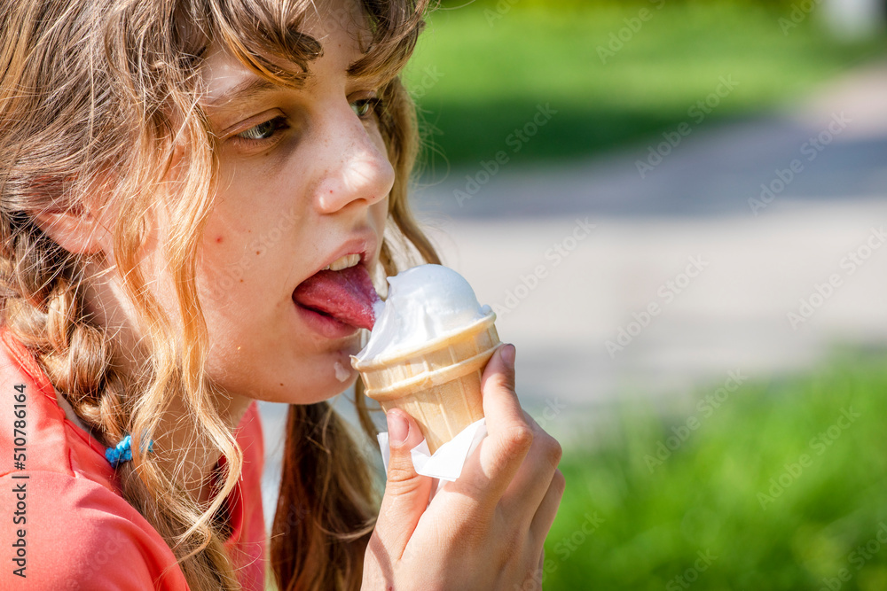happy teen girl licks natural ice cream with her tongue on a walk on a sunny day in profile with space for text - obrazy, fototapety, plakaty 