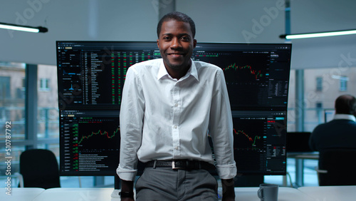 Schilderij op canvas Happy African-American trader smiling at camera leaning on desk with multi-scree