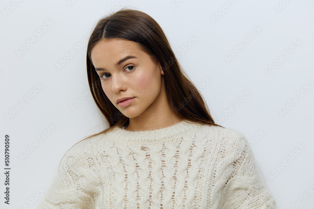 a beautiful, attractive woman in a white autumn, warm sweater stands on a light background looking pleasantly into the camera and smiling gently a beautiful, attractive woman in a white autumn, warm sweater stands on a light background looking pleasantly into the camera and smiling gently