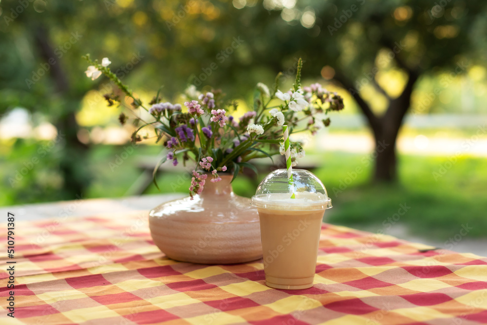 Cold iced coffee with milk on table. Cold summer drink in garden. Caramel frappe coffe in street coffee shop. Bouquet of summer flowers in ceramic vase on terrace. Cozy home decor of patio yard