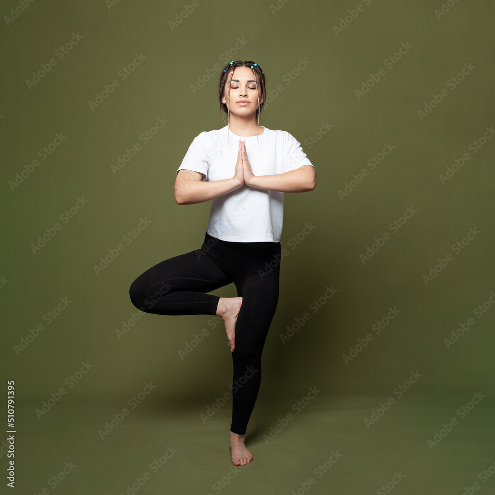 Beautiful young woman working out indoors, doing yoga exercise against green studio wall background, full length portrait