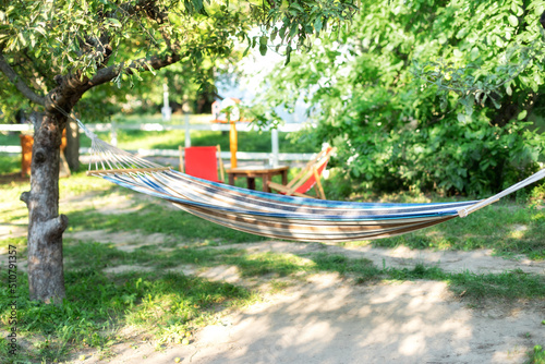Cozy place for weekend relax in yard. Hammock hanging on tree. Cozy exterior backyard. Concept of recreation outdoor. Comfortable Hammock hanging on tree in summer garden. 