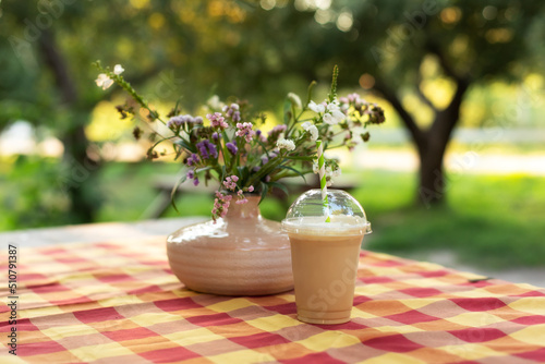 Cold iced coffee with milk on table. Cold summer drink in garden. Caramel frappe coffe in street coffee shop. Bouquet of summer flowers in ceramic vase on terrace. Cozy home decor of patio yard