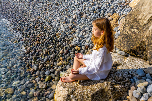 Beautiful little girl sitting on a rock by the sea and meditate. High quality photo