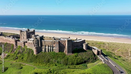 Aerial footage the famous Bamburgh Castle, a castle on the northeast coast of England, by the village of Bamburgh in Northumberland showing a drone view of the castle and sandy beach in the summer. photo