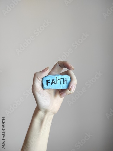 hand and holding blue painted rock with word faith 