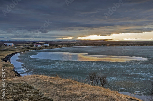 View across lake Myvatn in Iceland  partly frozen under dark clouds with a strip of clear sky and sunlight at the horizon