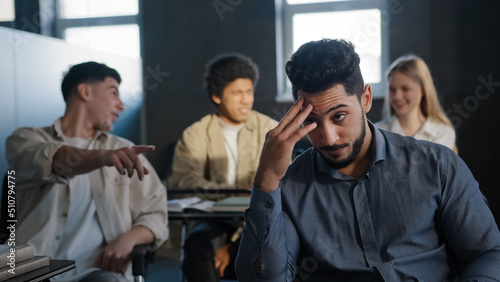 Young excited arab guy student sitting in classroom cannot concentrate on lesson being ridiculed by classmates suffering from abuse feeling distressed lonely upset concept of discrimination and racism