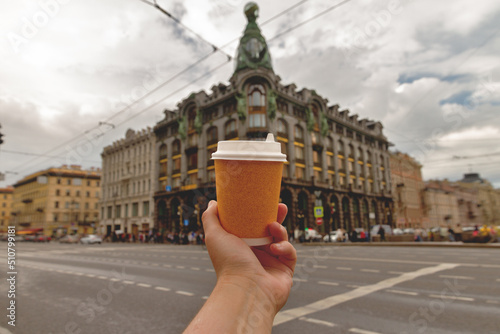 paper cup of natural coffee in women's hand against backdrop of the Singer House on Nevsky Prospekt in the center of St. Petersburg, Russia photo