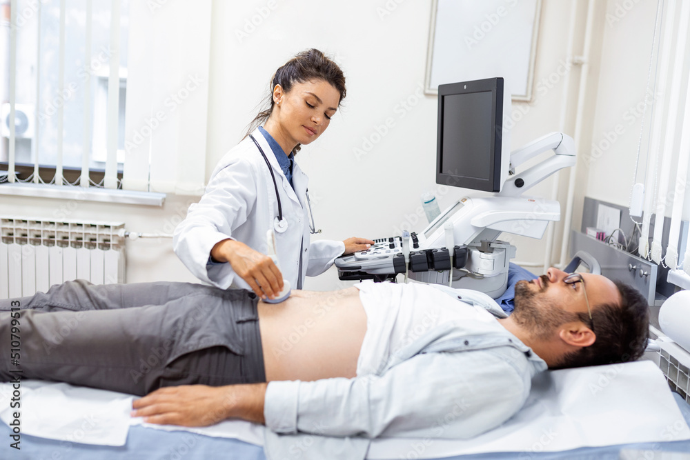 Obraz premium Ultrasound diagnosis of the stomach on the abdominal cavity of a man in the clinic, close-up view. The doctor runs an ultrasound sensor over the patient's male abdomen. Diagnostics of internal organs.
