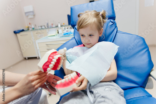 dentist teaches little girl patient to brush teeth