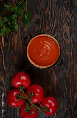 Tomato soup in a black bowl on brown background. Top view.