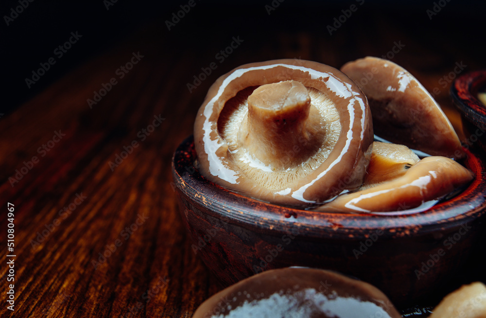 Beautiful delicious pickled mushrooms in a clay cup on a wooden table . Beautiful delicious pickled mushrooms in a clay cup on a wooden table .
