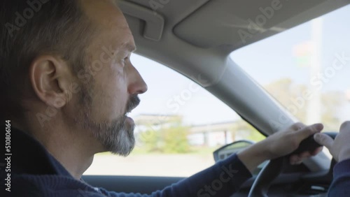 A middle-aged handsome Caucasian man acts angry in a road rage as he drives a car on a highway - side closeup