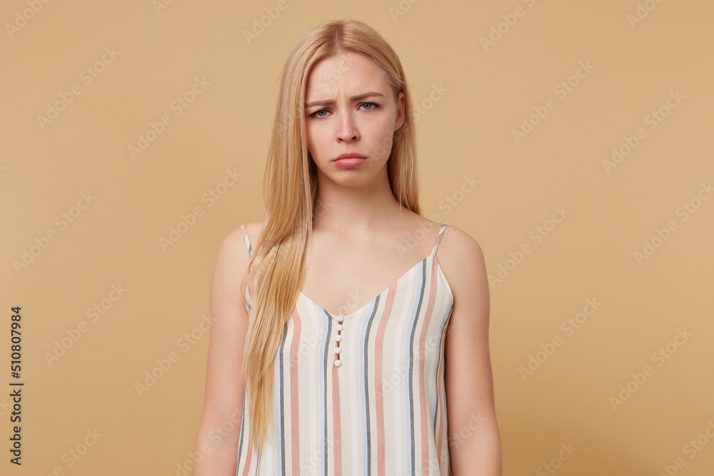 Obraz premium Studio portrait of young blonde woman posing over beige background sadly looking into camera