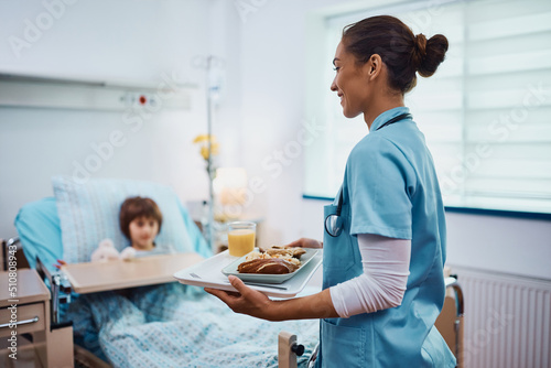 Valokuva Young pediatric nurse serving lunch to a child at hospital ward.