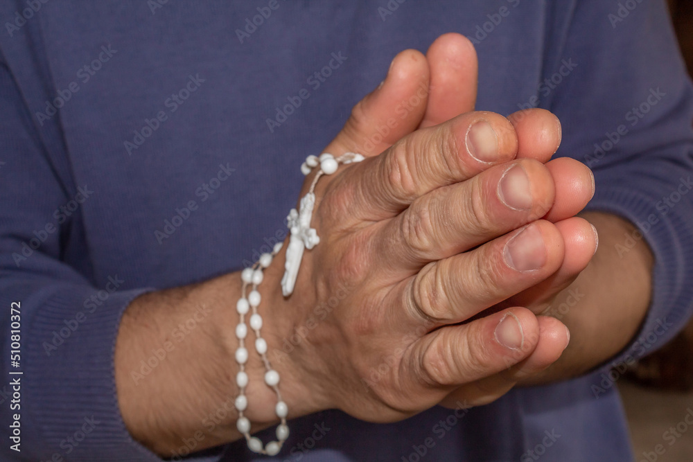 Hands folded in prayer. White cross on his hands. Believer in God