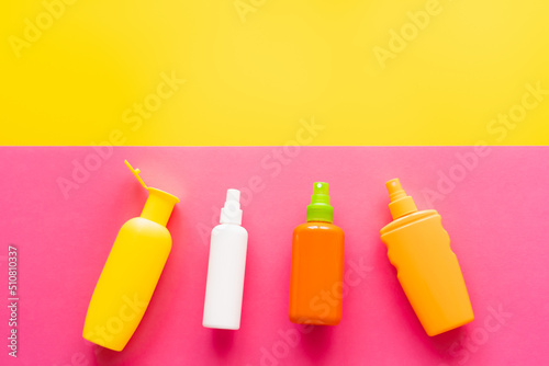 Top view of bottles of sunscreens on yellow and pink background.