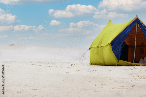 A tourist tent stands on the white sand on the beach. Summer tent for family outdoor recreation. camping  summer. Blue-yellow fabric. Active rest  family leisure away from civilization 
