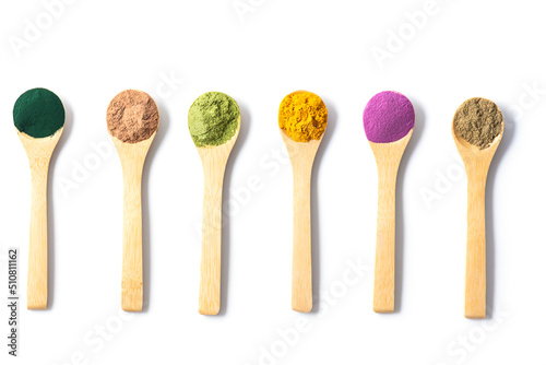 Superfood powders: sweet potato, matcha, spirulina, hemp, turmeric, carob in wooden spoons on a white background, flat lay, top view.
