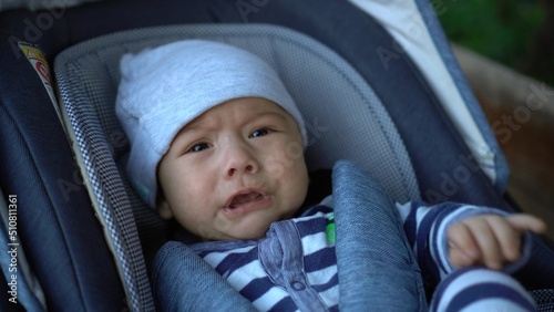 A newborn baby is crying while lying in a stroller. The child is unwell.