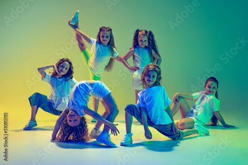 Photography Group of children, little girls in sportive casual style clothes dancing in choreography class isolated on green background in yellow neon light