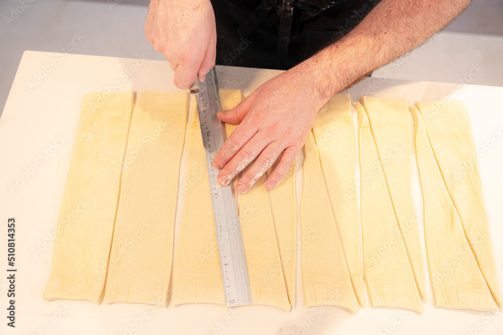Detail of the hands of a man cooking croissants making triangular cuts in the puff pastry, work at home Detail of the hands of a man cooking croissants making triangular cuts in the puff pastry, work at home