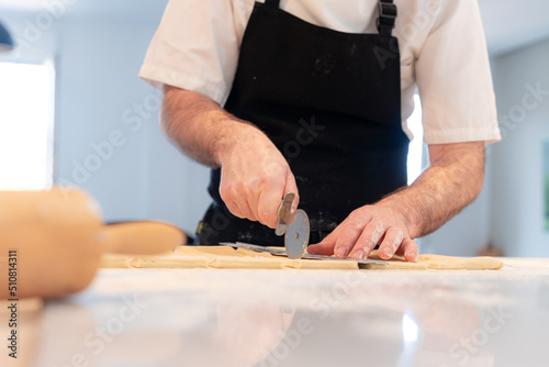 Detail of the hands of a man cooking croissants, measuring the puff pastry and making cuts, work at home