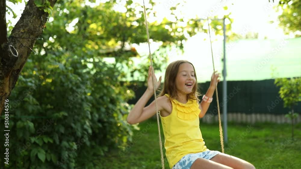 Happy barefoot laughing child girl swinging on a swing in sunset summer day on the backyard at home, summertime outdoor, vacation. Happy barefoot laughing child girl swinging on a swing in sunset summer day on the backyard at home, summertime outdoor, vacation.