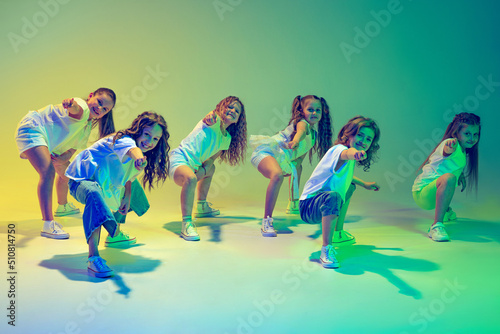 Group of children  little girls in sportive casual style clothes dancing in choreography class isolated on green background in yellow neon light. Concept of music  fashion  art