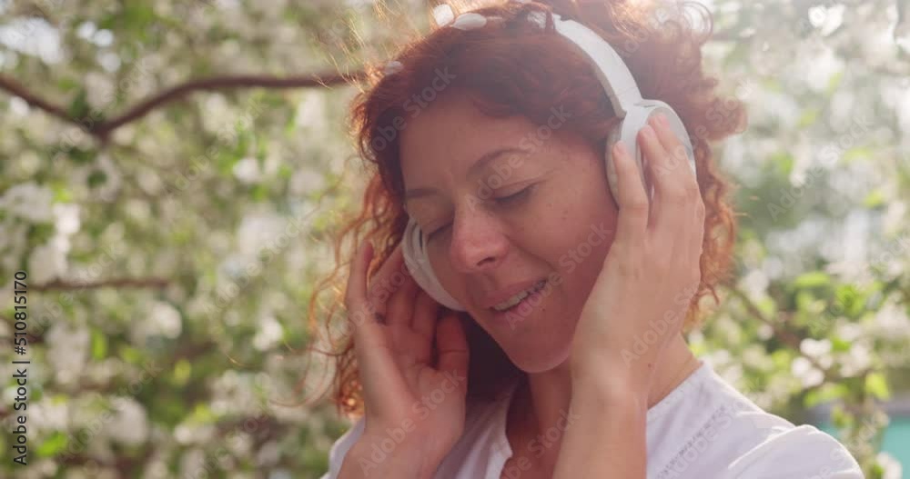 Red-haired woman in headphones in a flowering garden listening to music while dancing Red-haired woman in headphones in a flowering garden listening to music while dancing