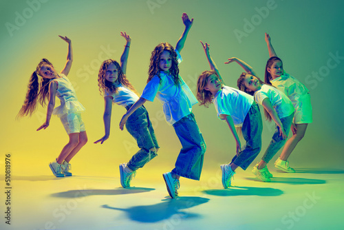 Fototapeta Naklejka Na Ścianę i Meble -  Group of children, little girls in sportive casual style clothes dancing in choreography class isolated on green background in yellow neon light. Concept of music, fashion, art