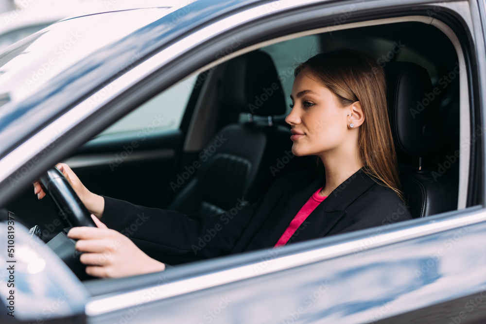 Happy woman driving a car and smiling. Cute young success happy brunette woman is driving a car. Portrait of happy female driver steering car with safety belt