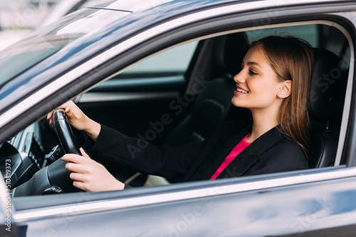 Happy woman driving a car and smiling. Cute young success happy brunette woman is driving a car. Portrait of happy female driver steering car with safety belt © F8  \ Suport Ukraine