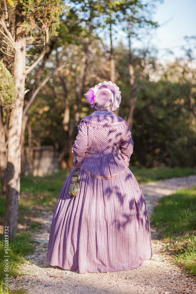 Woman in victorian dress walking in the park. Vintage fashion.