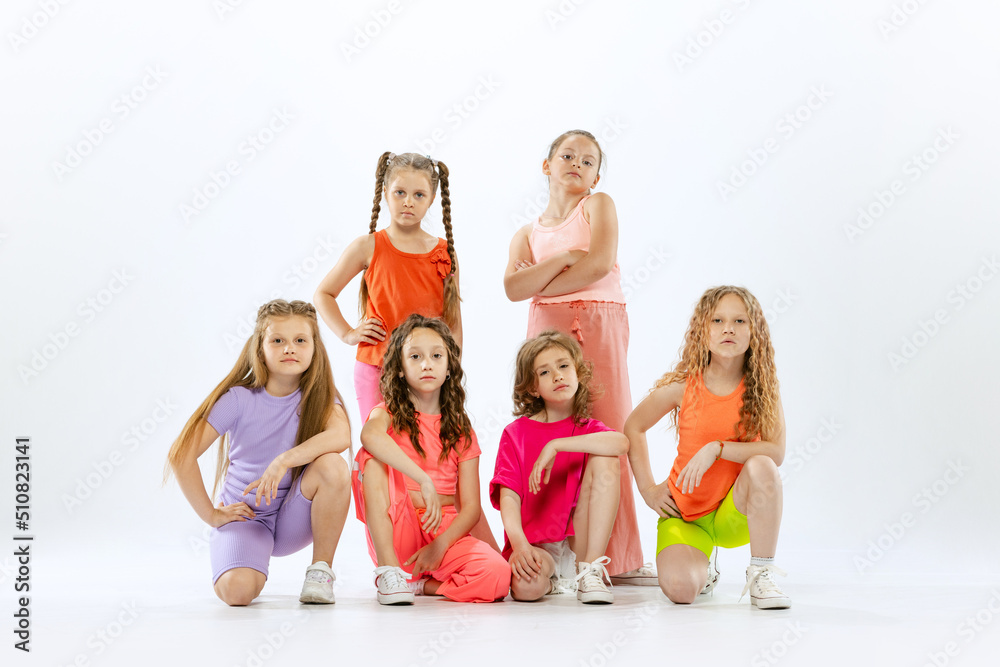 Dance group of happy, active little girls in bright colorful clothes dancing isolated on white studio background. Concept of music, fashion, art, childhood, hobby