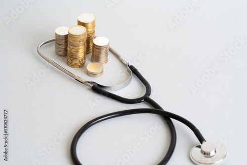 Close up photo of stethoscope and stacked coins on isolated background. Concept of rising costs of healthcare expenses. Selective focus.