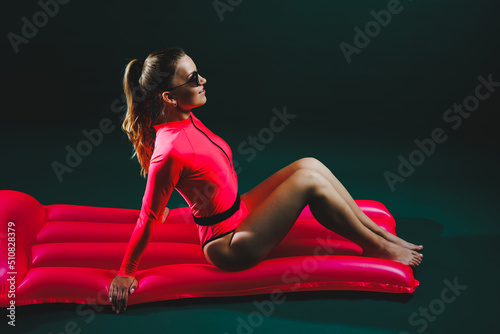Young attractive woman slim body in sunglasses and in a pink swimsuit lies on an inflatable mattress isolated on a green background. Summer vacation vacation at sea tanning concept. Pink air mattress