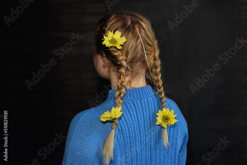 Ukrainian girl in blue with yellow flowers in her braids. Isolated on dark , from the back. No face. Colors of Ukraine.