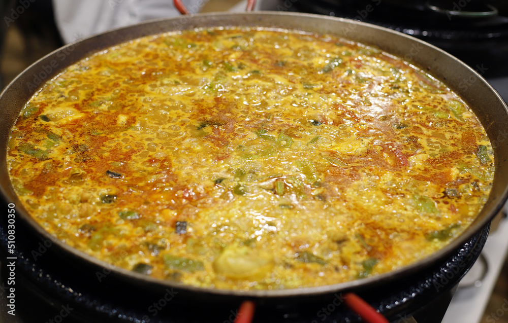 Paellera en los fogones cociendo arroz con verduras