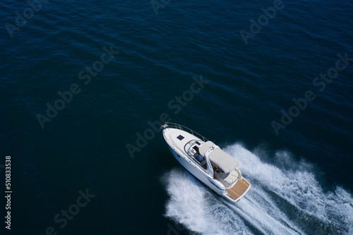 A large white boat at high speed on the water leaves a white trail, top view. White yacht fast moving on clear water aerial side view.