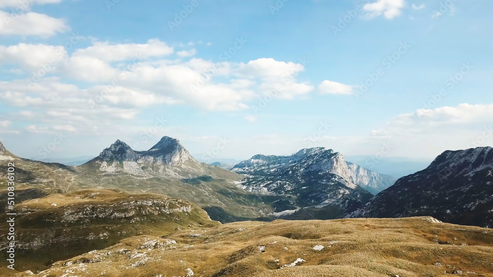 Top view of mountain panorama against blue sky. Stock. Rocky peaks of mountains with cover of grass at foothills create beautiful landscape