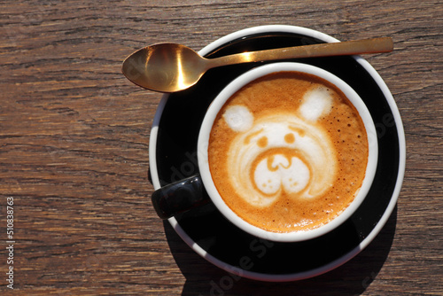 Latte art, drawing of the bear’s face, coffee art made by barista with a golden spoon on wooden background table, view from above or top. Copy space for text on the left side.  photo