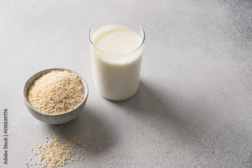 Vegan plant based Sesame milk and white sesame seeds on gray background. Close up. Healthy vegetarian beverage. Copy space. Vegan plant based Sesame milk and white sesame seeds on gray background. Close up. Healthy vegetarian beverage. Copy space.