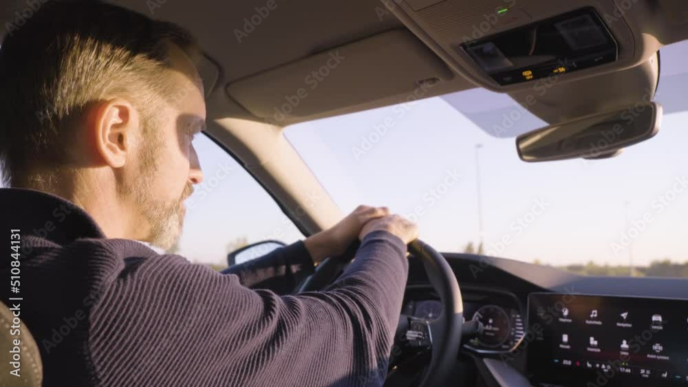 A middle-aged handsome Caucasian man drives a car on a road - rear closeup from the backseat A middle-aged handsome Caucasian man drives a car on a road - rear closeup from the backseat