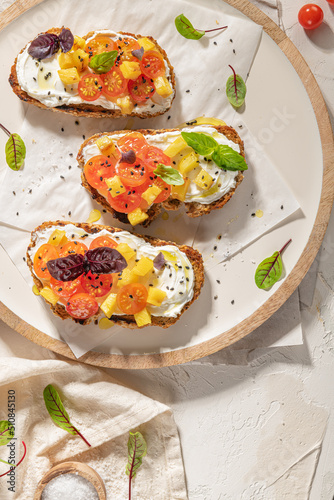 Italian bruschettas with roasted tomatoes, cream cheese, pineapple slices and herbs on a kitchen countertop. Prepared to serve