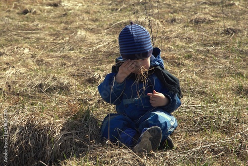 a two-year-old boy plays outside in the spring, dressed in blue
