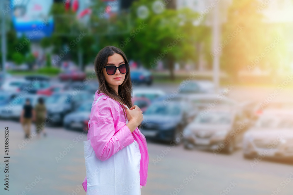 Street portrait of pretty girl with white shopping bag. Young woman on cityscape background.
